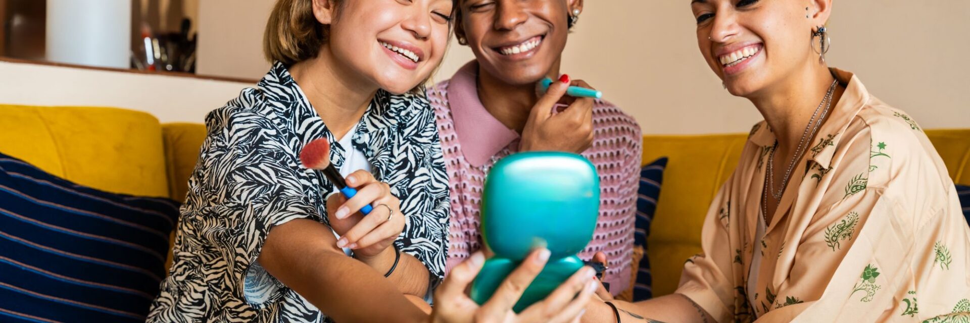 Group of LGBTQ+ young people on a sofa putting on makeup