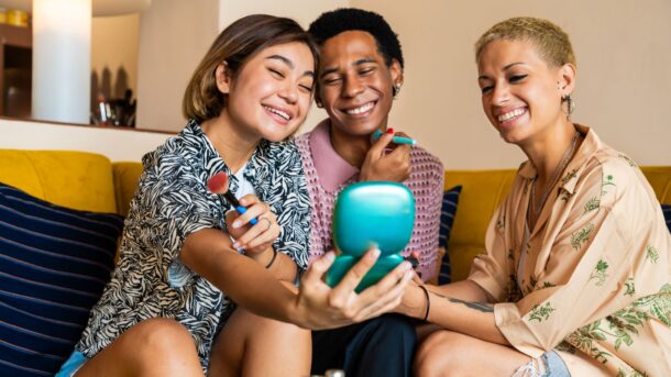 Group of LGBTQ+ young people on a sofa putting on makeup