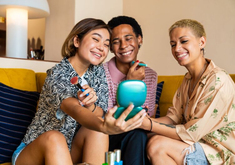 Group of LGBTQ+ young people on a sofa putting on makeup